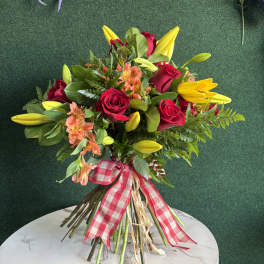 Bouquet of red roses, yellow lilies, and peach flowers tied with a gingham ribbon