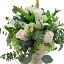 White roses and lilies arranged with green succulents in a vase
