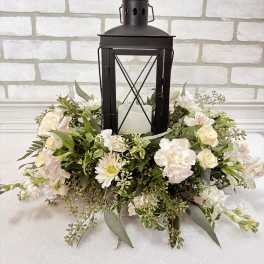 White floral wreath around a black lantern with a candle inside