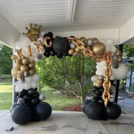 Black, white, and gold balloon arch with a crown and "KING" letters