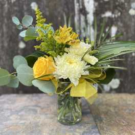 Yellow and white flower arrangement in a glass vase with ribbon