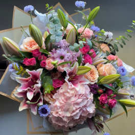 Mixed bouquet with pink lilies, roses, hydrangea, and blue accent flowers