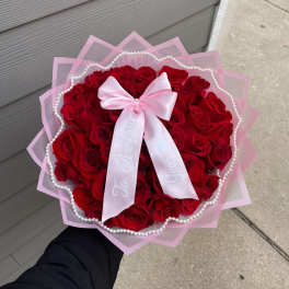 Round bouquet of red roses wrapped in pink paper with a satin bow