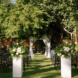 Outdoor wedding aisle with white floral arrangements and a draped arch