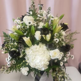 White and black floral arrangement in a white vase with lilies, roses, and hydrangea