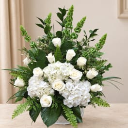 White roses and hydrangeas in a low vase with green foliage