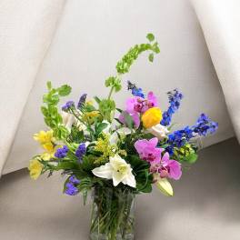 Mixed bouquet of lilies, orchids, roses, and blue flowers in a glass vase
