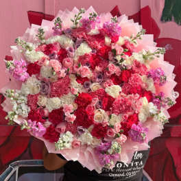 Large bouquet of pink, red, and white flowers wrapped in pale pink paper