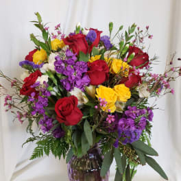 Mixed bouquet of red, yellow, and purple flowers in a purple glass vase