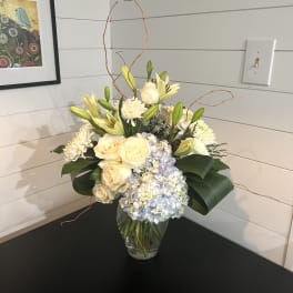 Cream roses, lilies, and blue hydrangeas in a glass vase