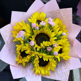 Bouquet of yellow sunflowers with small pink spray roses in pink paper