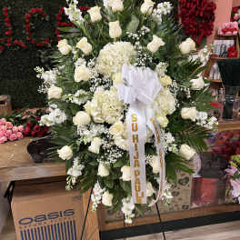 Large standing spray of white roses and hydrangeas with ribbons on a black easel