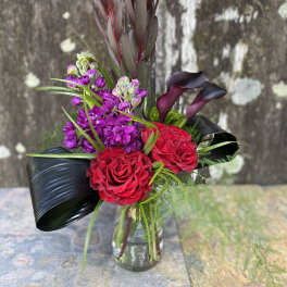 Bouquet of red roses, purple flowers, and dark calla lilies in a glass vase