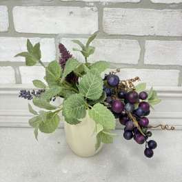 Small faux floral arrangement with purple berry clusters in a cream vase