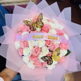 Round bouquet of pink and white roses wrapped in pink mesh with gold butterfly accents and HOCO 2024 ribbon.