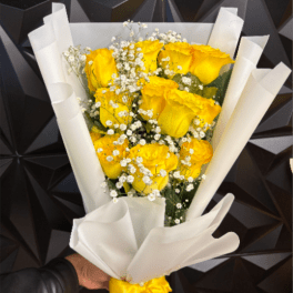 Bouquet of yellow roses with white filler flowers wrapped in white paper and tied with a yellow ribbon
