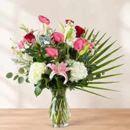 Pink lilies, red roses, and white hydrangeas in a glass vase with a birthday sign