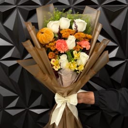Bouquet of white roses, orange chrysanthemums, and pink carnations wrapped in brown paper