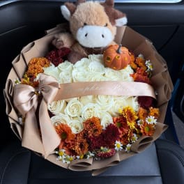 Bouquet of white roses and autumn flowers with a plush cow and pumpkin