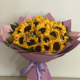 Bouquet of yellow sunflowers wrapped in pink paper with a lavender ribbon