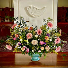 Large mixed pastel flower arrangement in a turquoise pedestal bowl before a white pulpit.