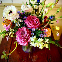 Mixed bouquet with pink roses, white ranunculus, purple iris, and small asters in a glass vase
