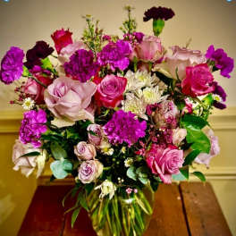 Mixed bouquet of pink and purple roses, carnations, and white daisies in a clear glass vase