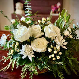 Low arrangement of white roses and mums in a basket with abundant evergreens.