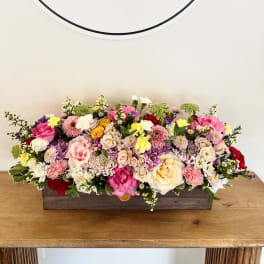 Low floral centerpiece in a rectangular wooden box with pink, white, and yellow blooms