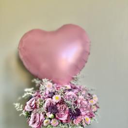 Pink heart balloon above a pink flower box arrangement