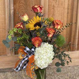 Bouquet of roses, sunflower, and white hydrangea in a glass vase