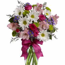 Mixed bouquet of daisies, roses, and alstroemeria in a glass vase with a magenta ribbon