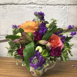 Colorful bouquet of orange and purple flowers in a floral ceramic pitcher