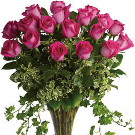 Pink roses arranged in a clear glass vase with trailing ivy