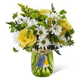 Yellow roses and white daisies with green accents in a green glass jar with a hello tag