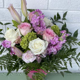 Pink and white roses with lilies and purple blooms in a glass vase