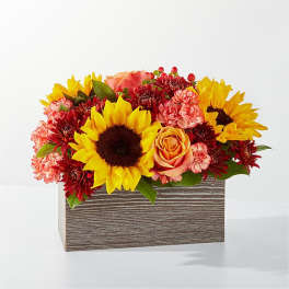 Sunflowers, roses, and carnations arranged in a striped rectangular box
