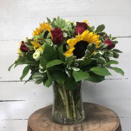 Sunflowers and red roses arranged in a clear glass vase