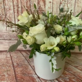 White floral arrangement in a white vase with roses and orchids