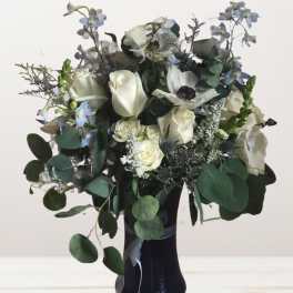 White roses and pale blue flowers in a black vase