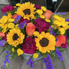 Bright mixed bouquet with sunflowers, roses, and purple blooms in a metal bucket