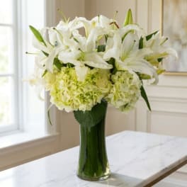 White lilies and pale green hydrangeas in a tall glass vase