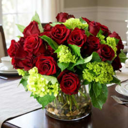 Red roses and green hydrangeas in a clear glass vase with pebbles
