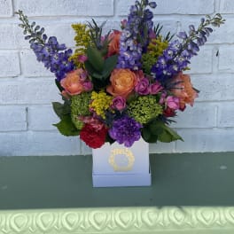Colorful bouquet of purple, peach, and pink flowers in a white box