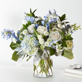 White roses and blue flowers in a clear glass vase