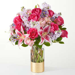 Pink roses and lilies arranged in a glass vase with a gold base