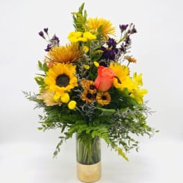 Mixed bouquet of yellow, purple, and coral flowers in a gold vase