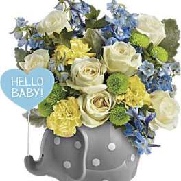 Bouquet of white roses, blue flowers, and yellow carnations in a gray elephant container