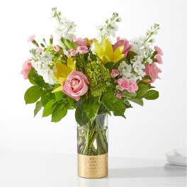 Pink roses and yellow lilies in a clear vase with a gold base