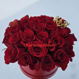 Red roses arranged in a round red box with a small crown decoration